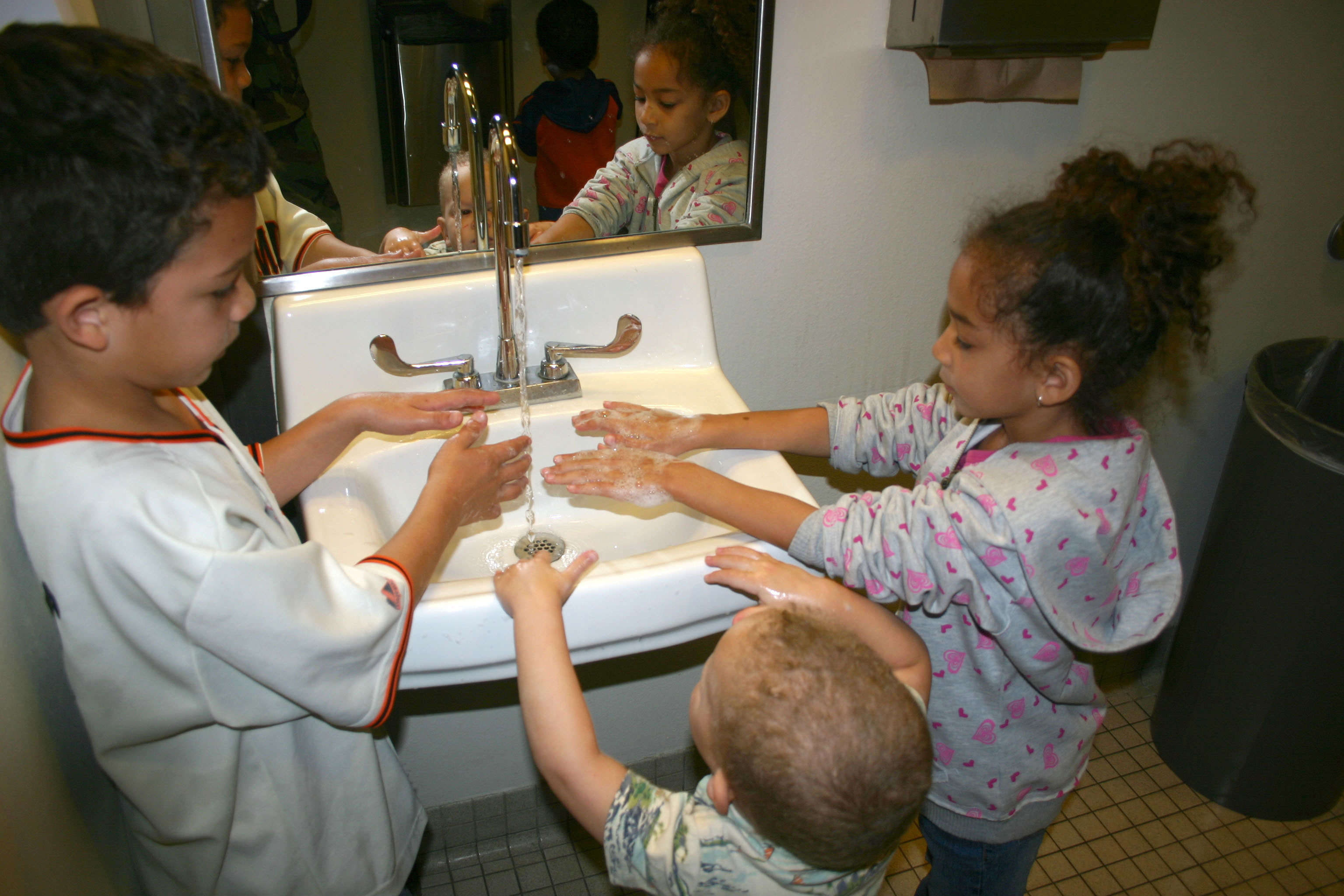 Three children washing their hands together in a bathroom sink.