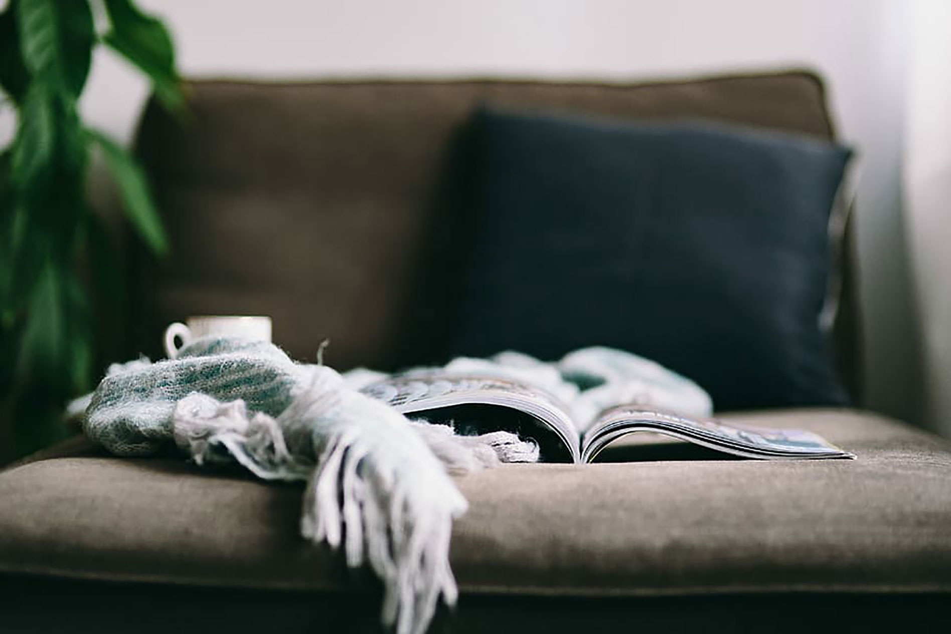 A blanket, book and cup of hot tea arranged on a sofa.