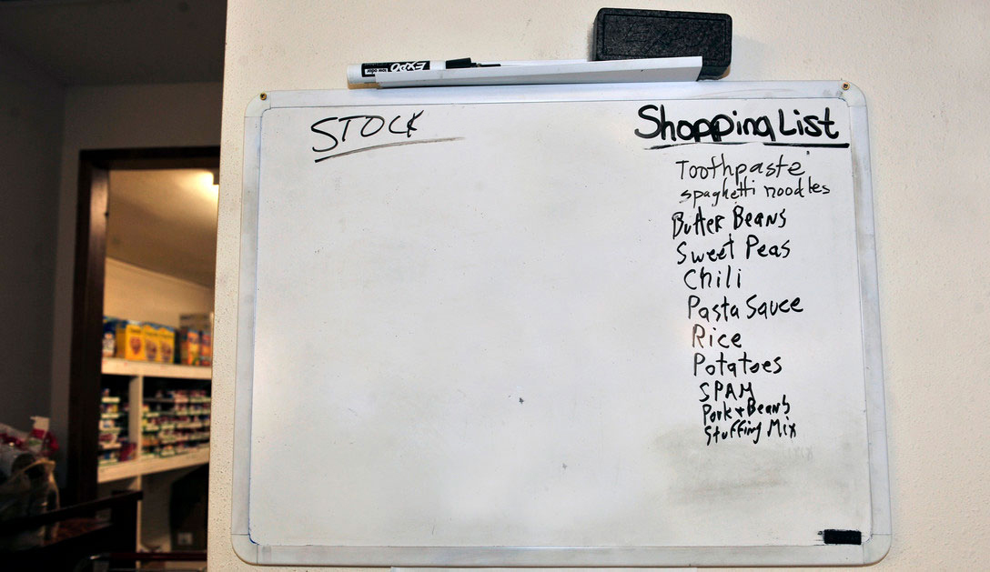 A whiteboard outside a home pantry with a shopping list and a stock list.