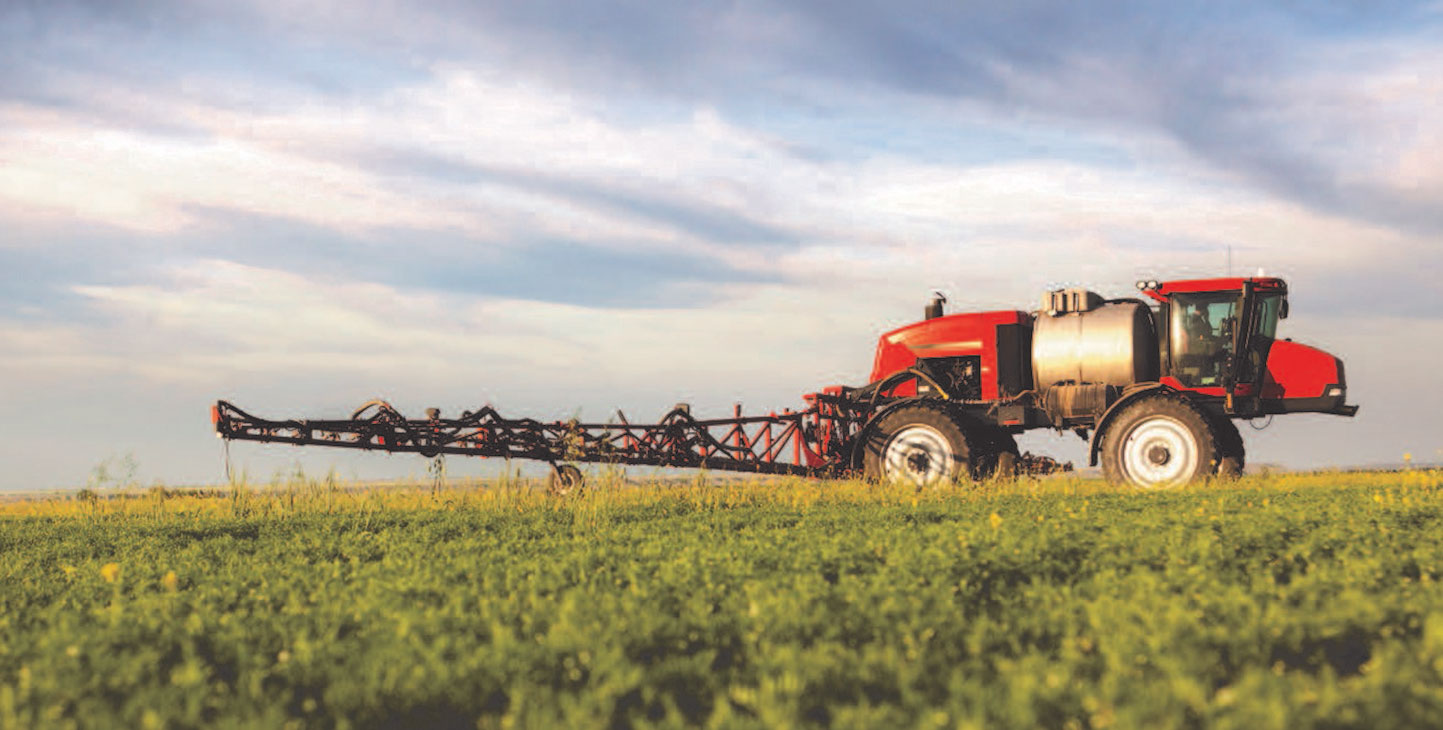 A red sprayer in a green field with a cloudy sky in the background.