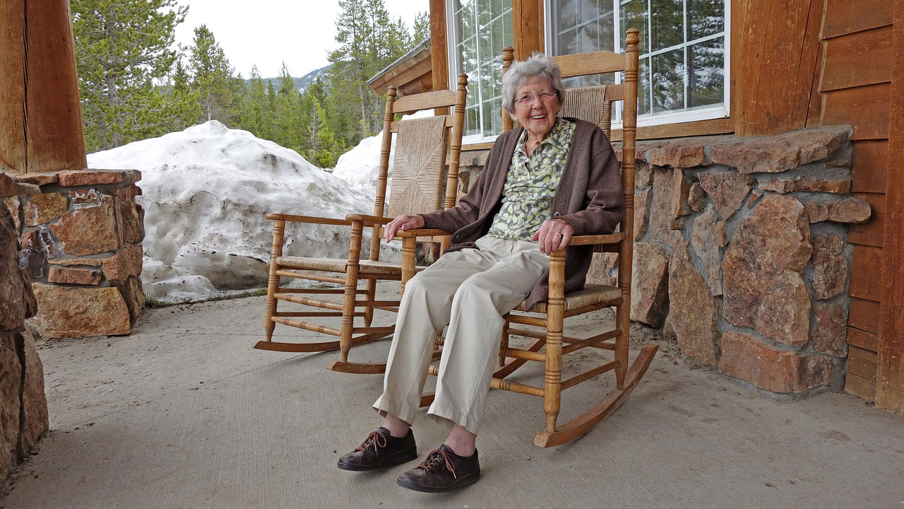 An older woman sitting on a front porch in a rocking chair.