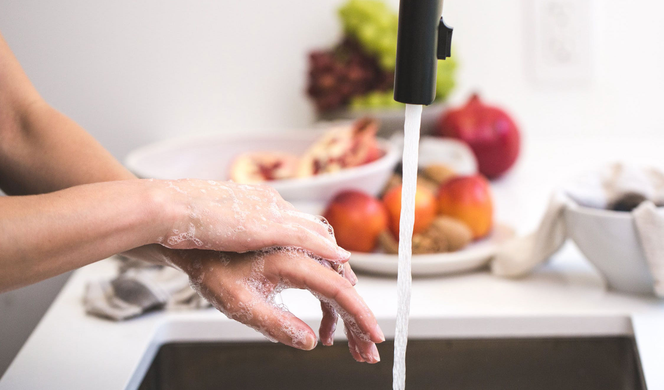 A woman washing her hands in the kitchen sink.