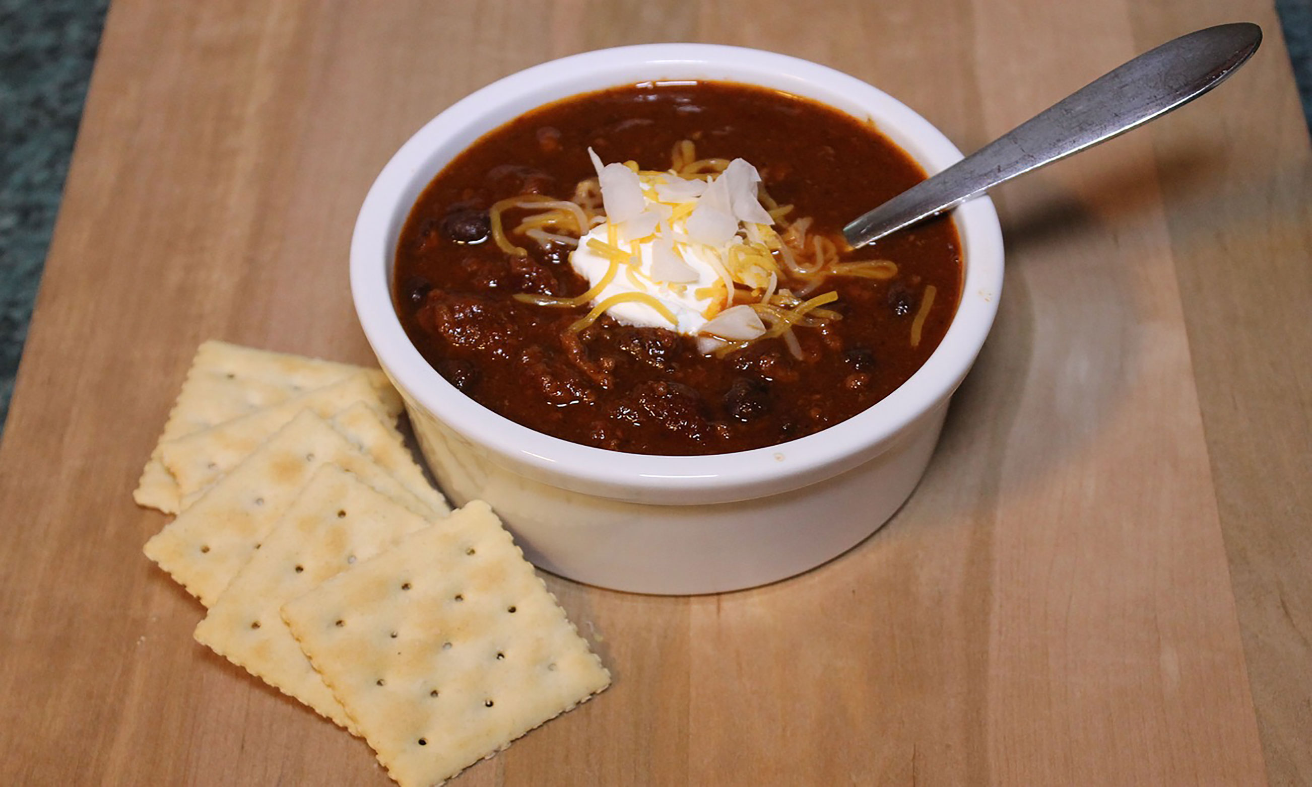 A bowl of chili topped with sour cream, onions, and cheese with saltine crackers on the side.