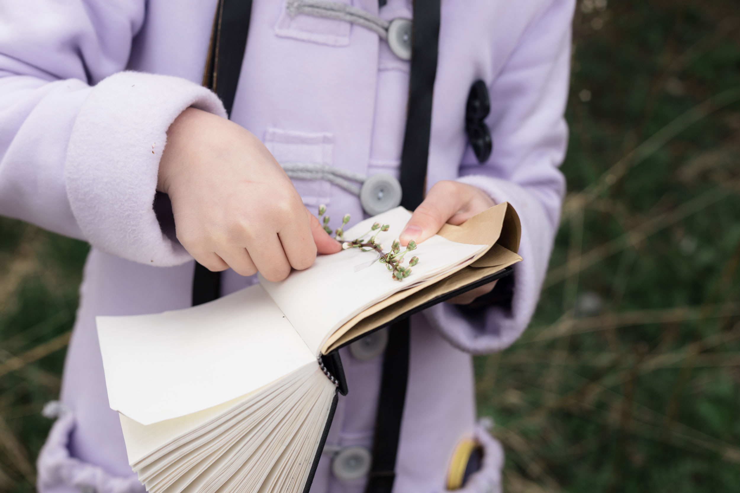 A young girl with a notebook observing a sprig of flower blossoms.