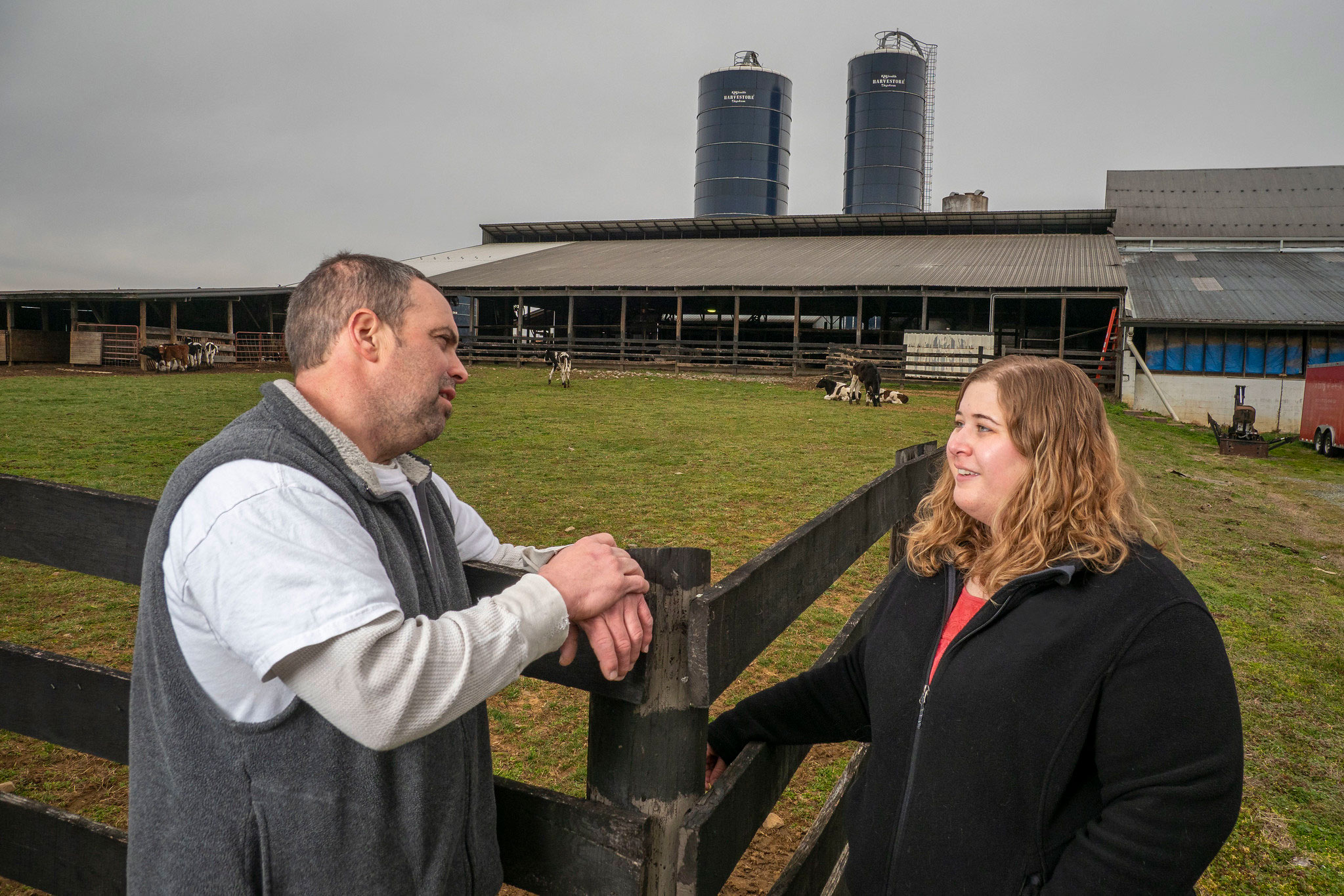 An dairy farmer and site inspector talking near a fence outside a dairy dairy barn.