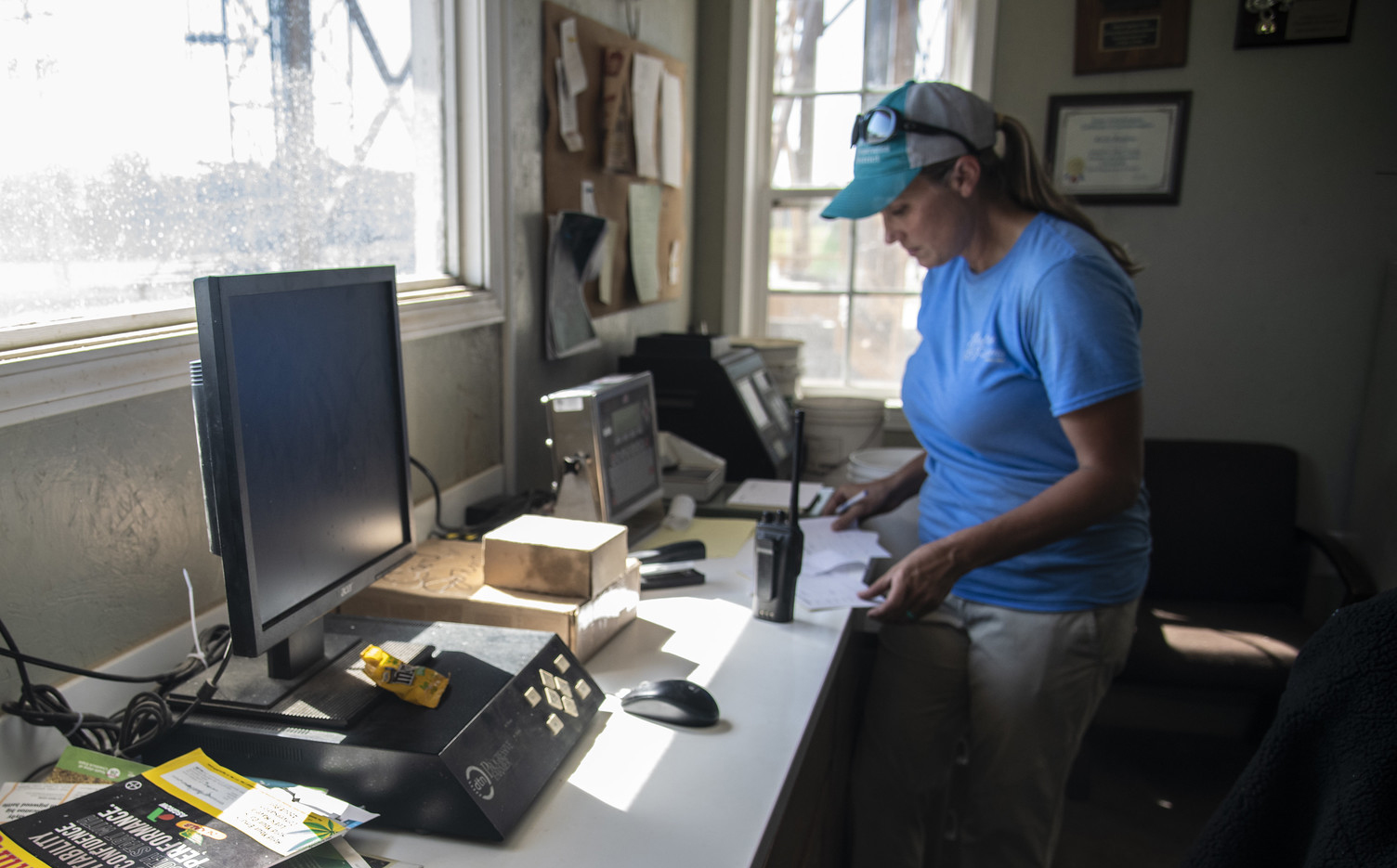 A female producer looking over paperwork in a farm office near a computer station.