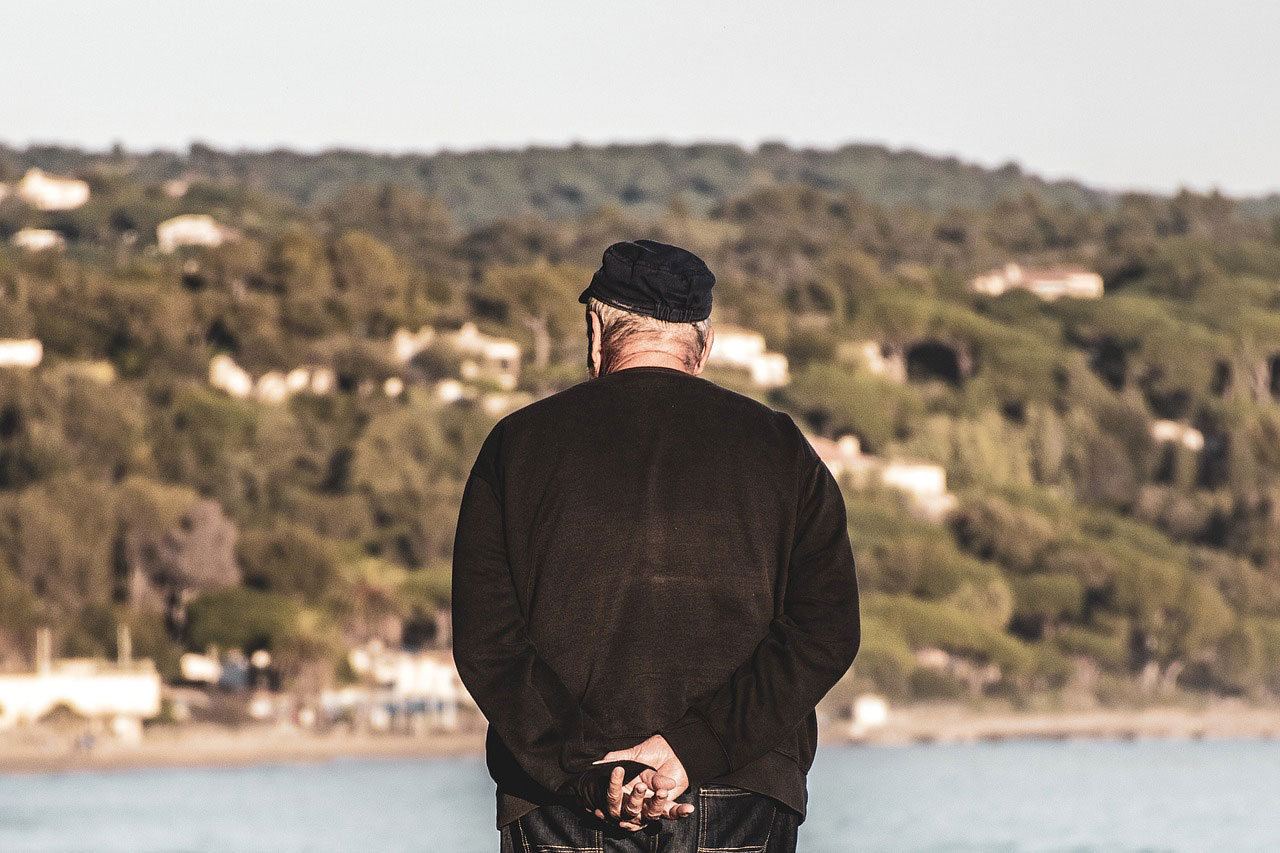 An older man with his back to the camera looking over a pond.