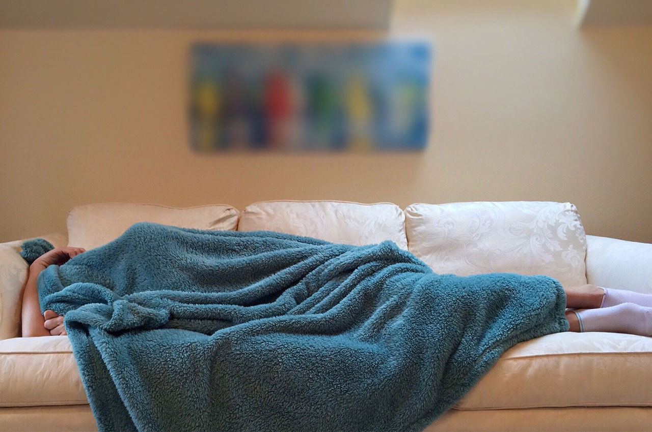 A person sleeping under a blue blanket on a white.