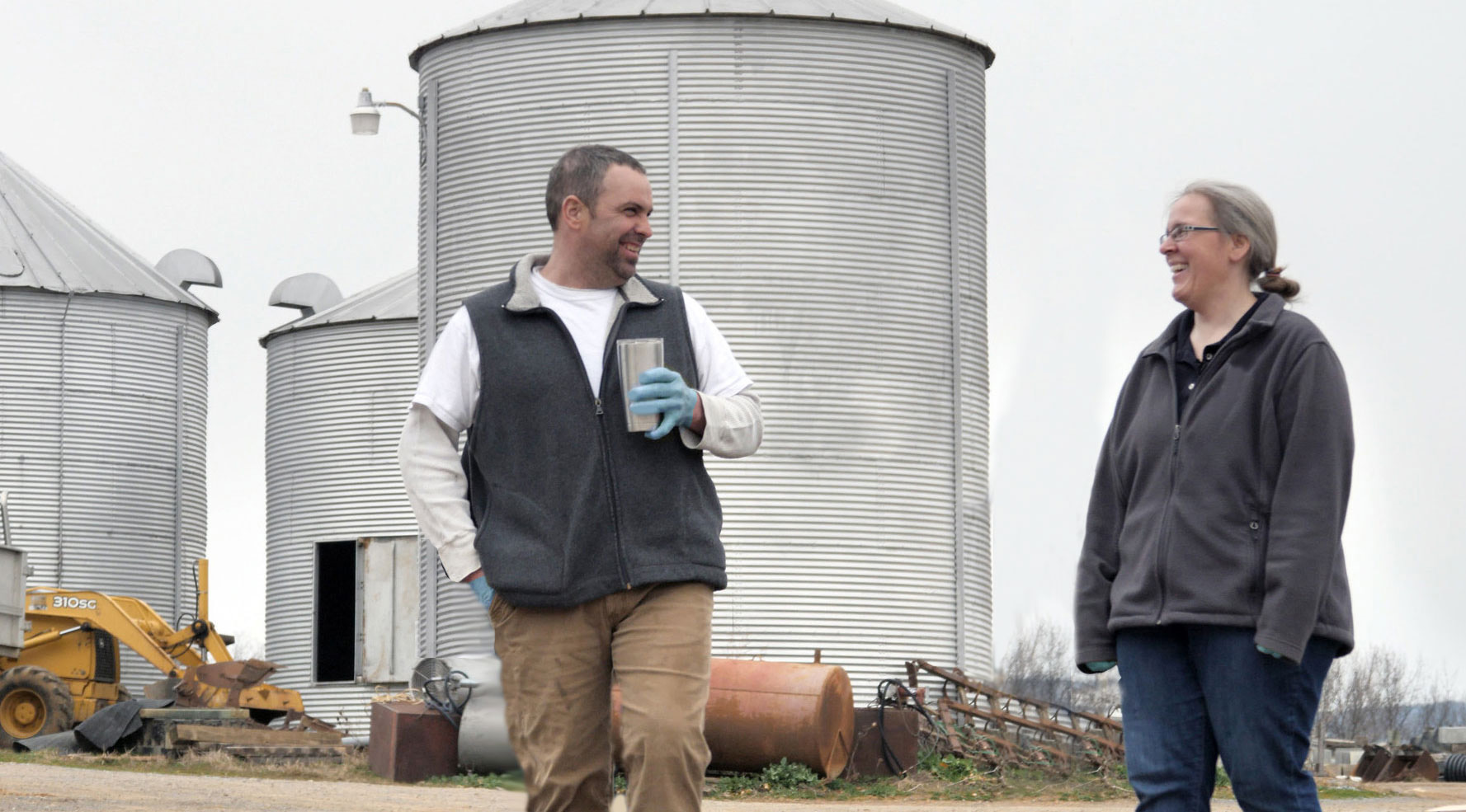 A producer meeting with an employee in a farmyard.