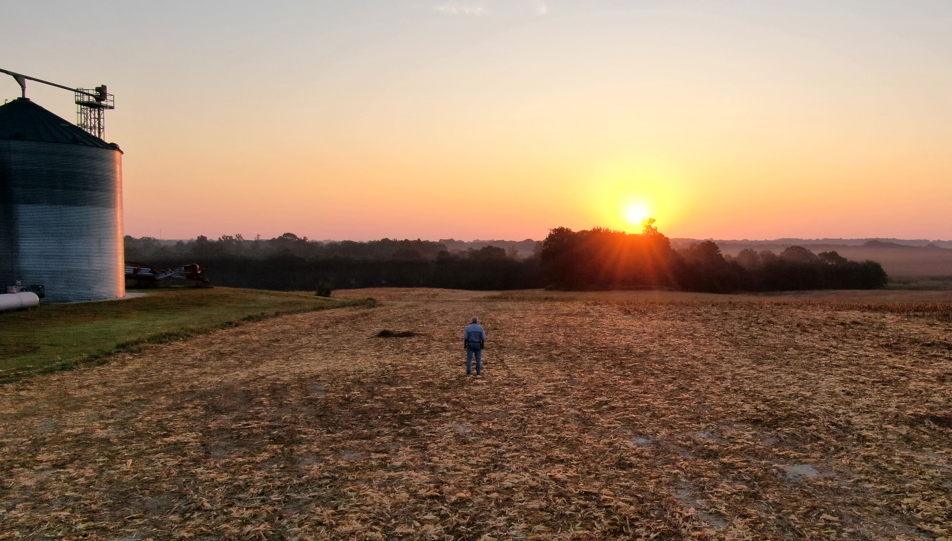 A farmer watching the sun rise in a bare, unplanted field.