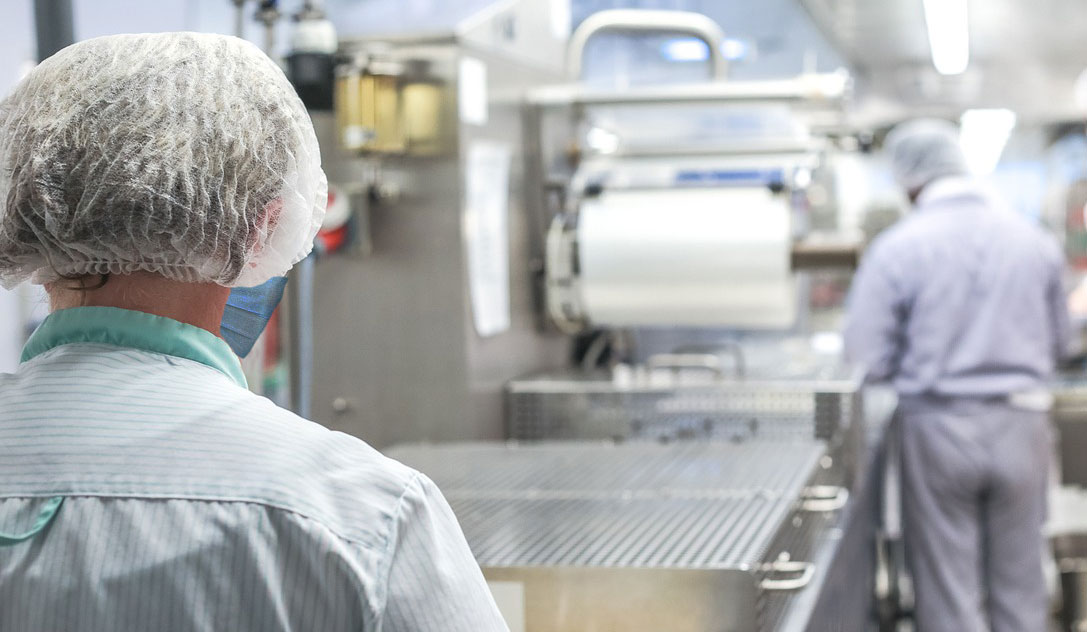 Two workers in protective clothing working in a commercial kitchen.