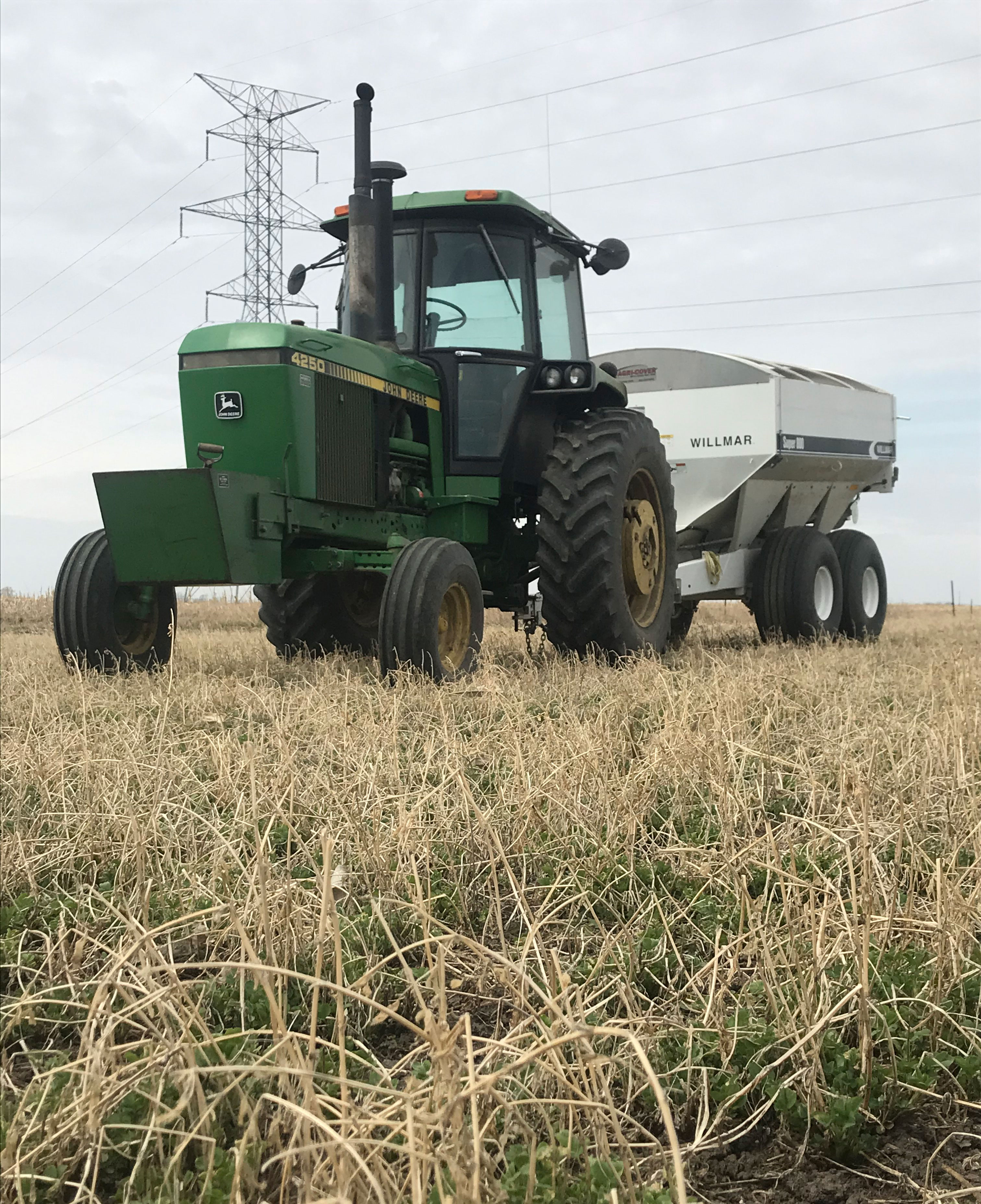 A green tractor pulling a fertilizer wagon through a field of alfalfa.