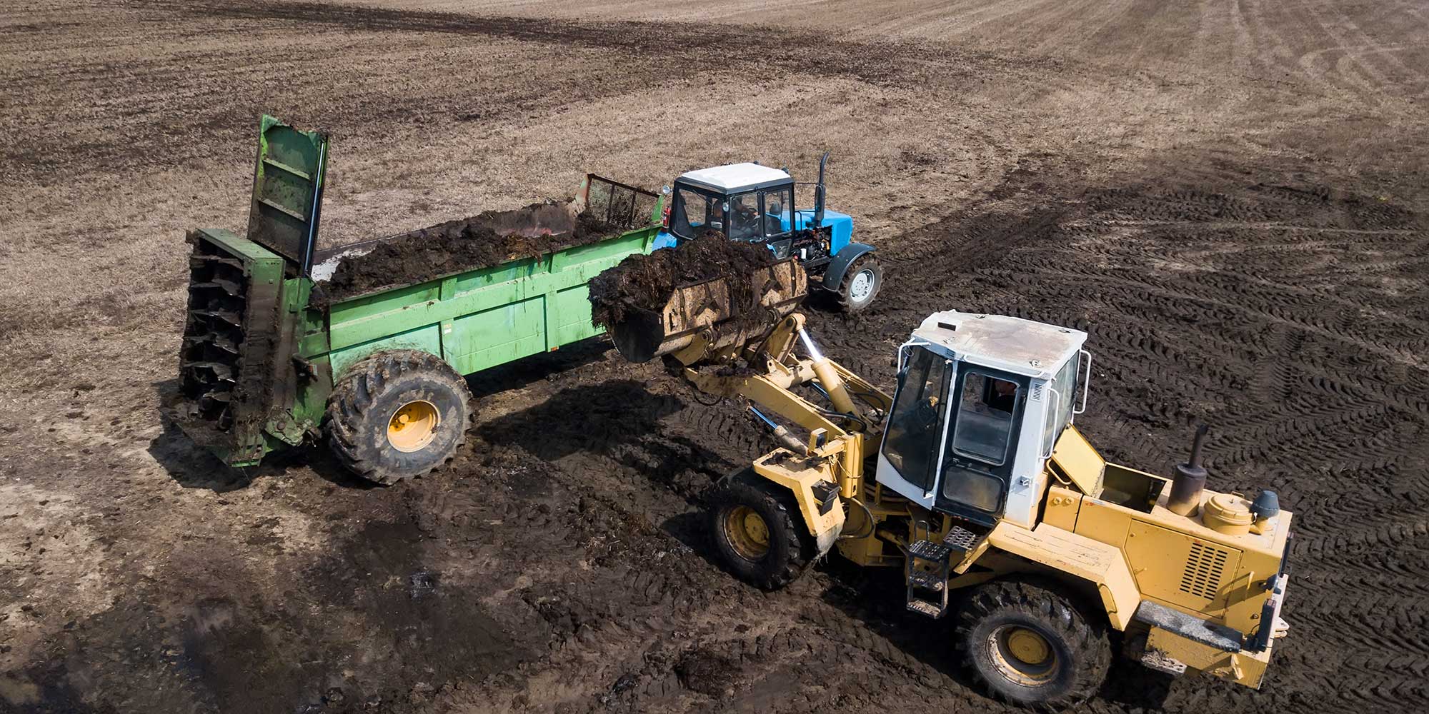 A loader depositing soil into a trailer being pulled behind a tractor.