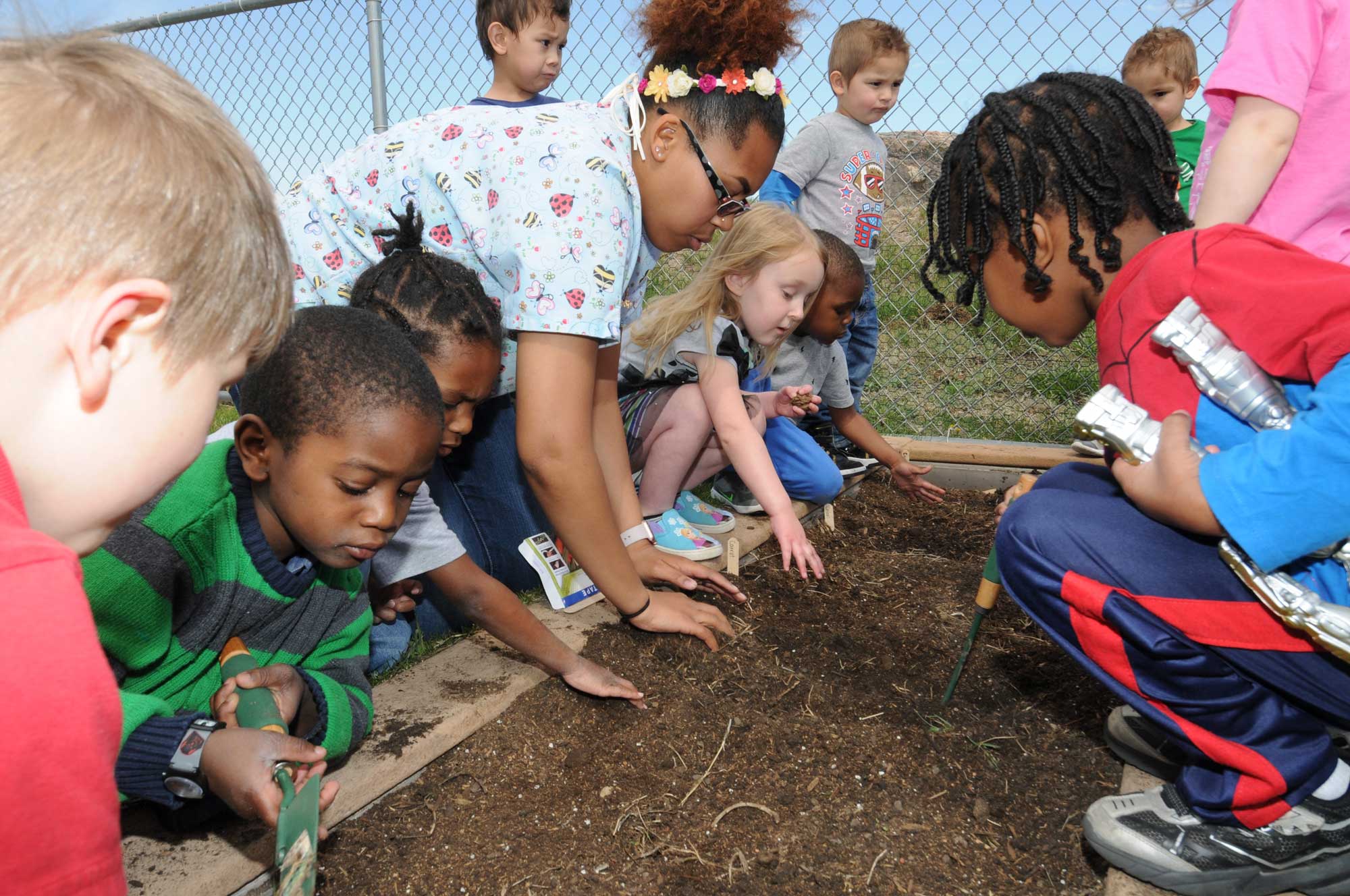 A group of children observing a bed of garden soil with a teacher.