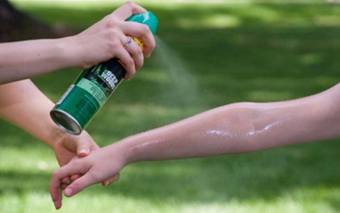 A woman applying bug spray to a teenager's arm.