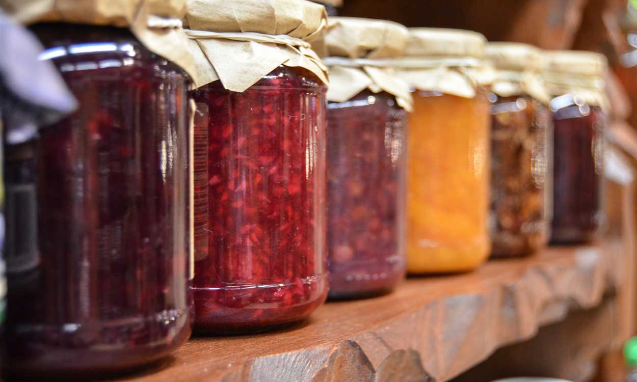 Several jars of canned jellies lined up on a pantry shelf.