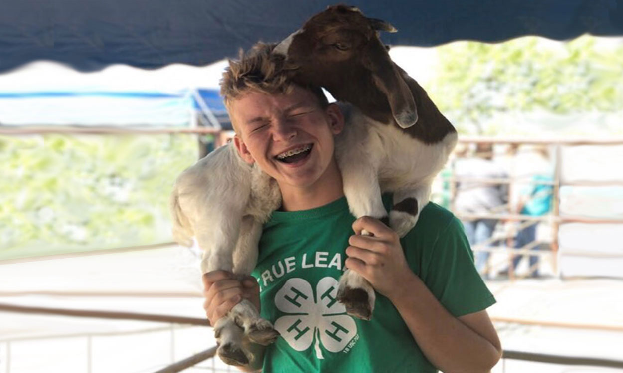 Carter Effling holding a goat over his shoulders at a 4-H event.