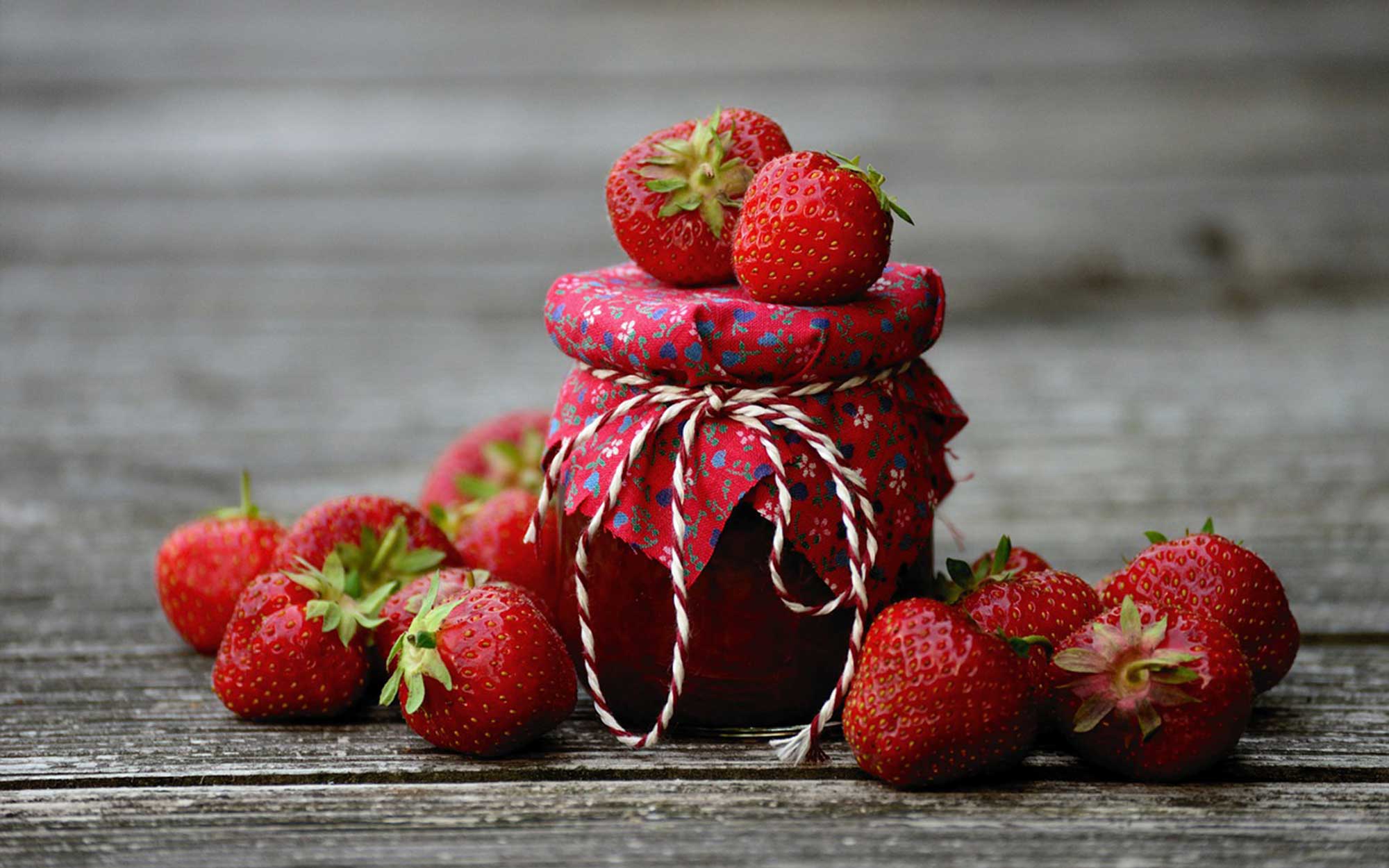 A jar of strawberry jam surrounded by fresh strawberries.