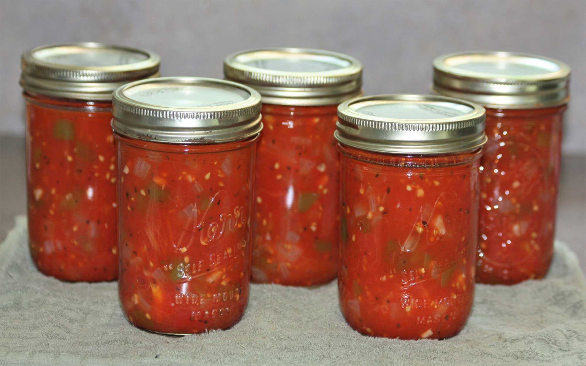 Five jars of canned salsa sitting on a countertop.