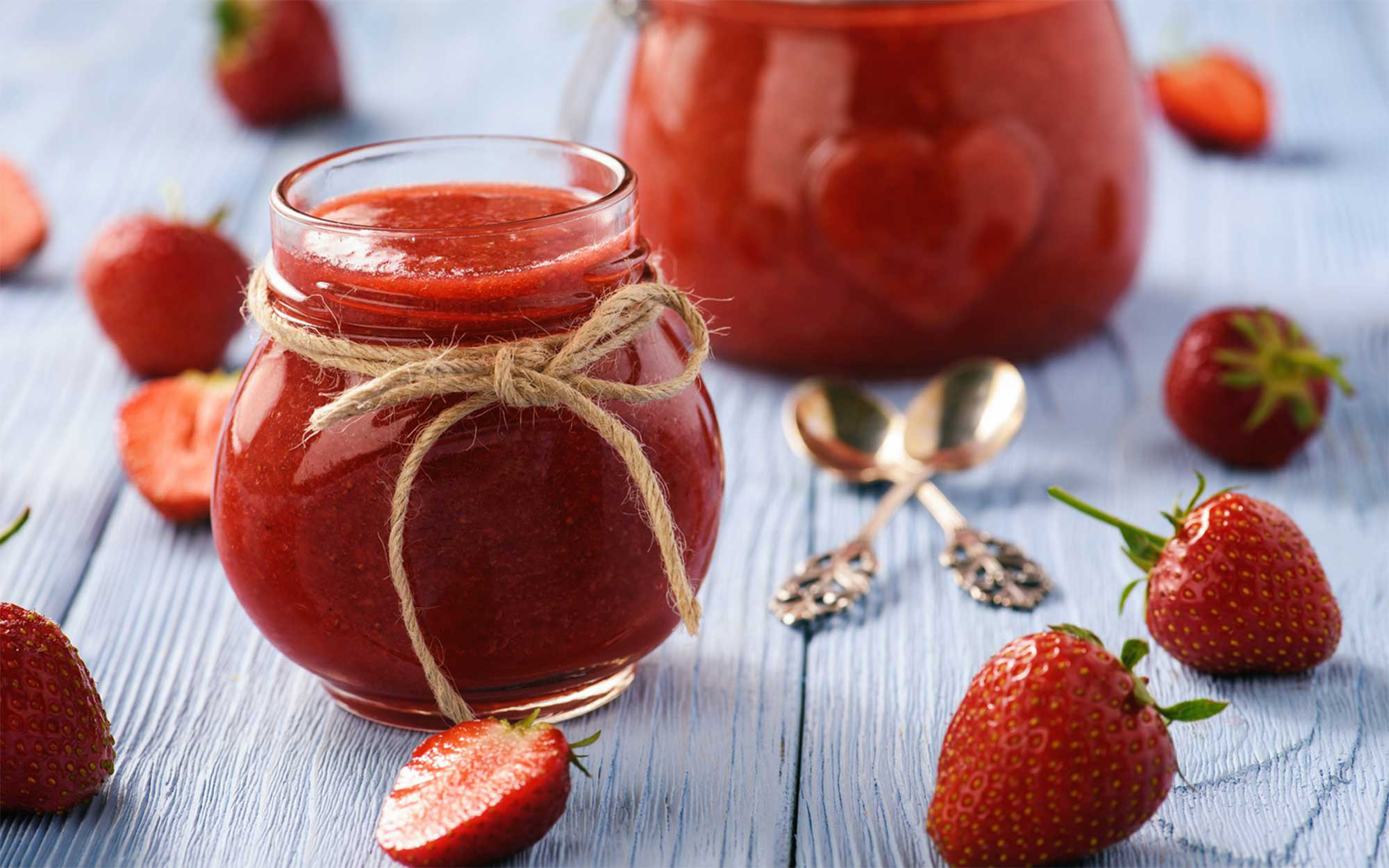 Two jars of freezer jam on a countertop with fresh strawberries.