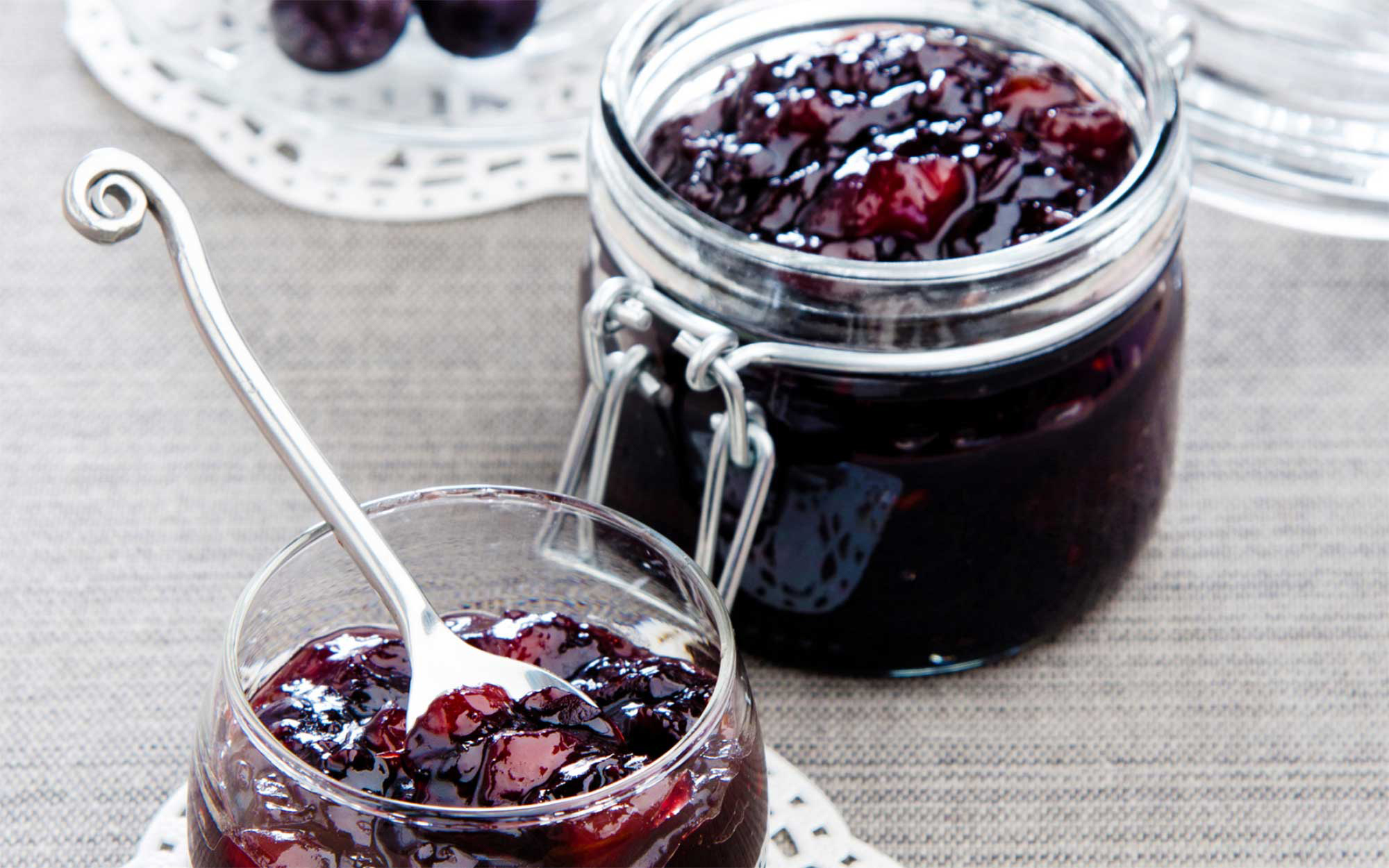 A jar of grape jelly and serving dish on a countertop.