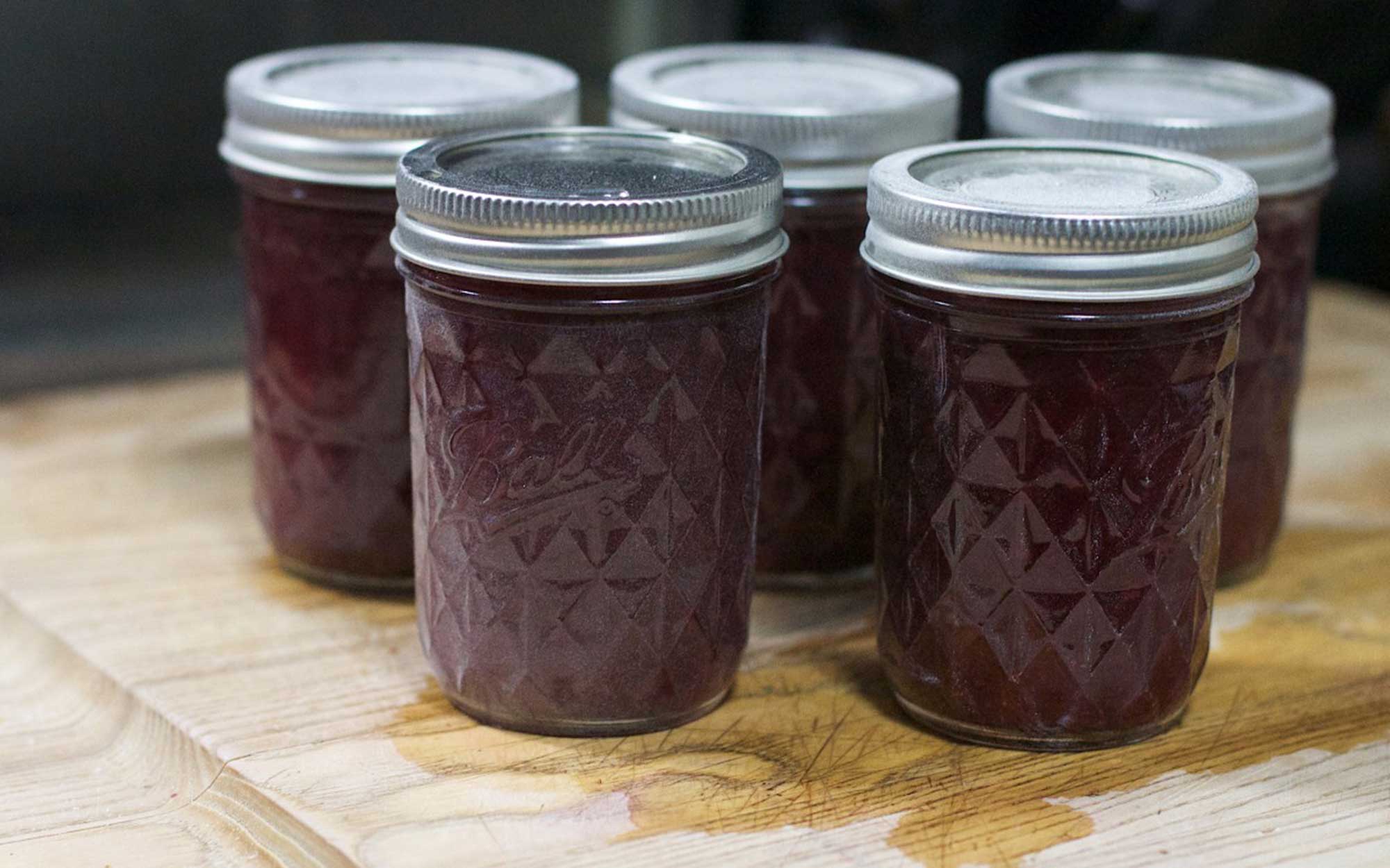 Five jars of reduced-sugar grape jam on a counter.
