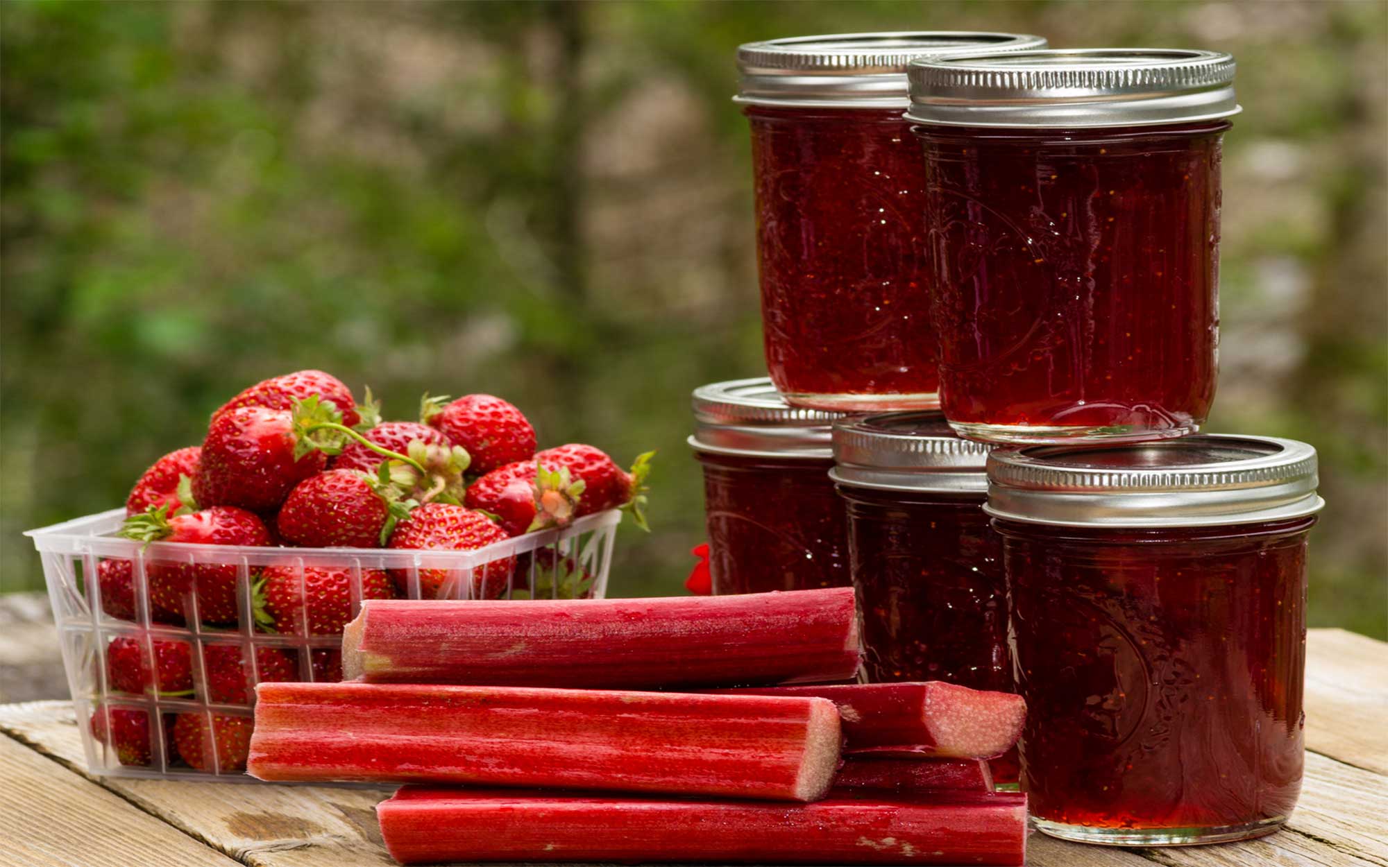 Strawberries, rhubarb, and five jars of strawberry-rhubarb jam on a picnic table.