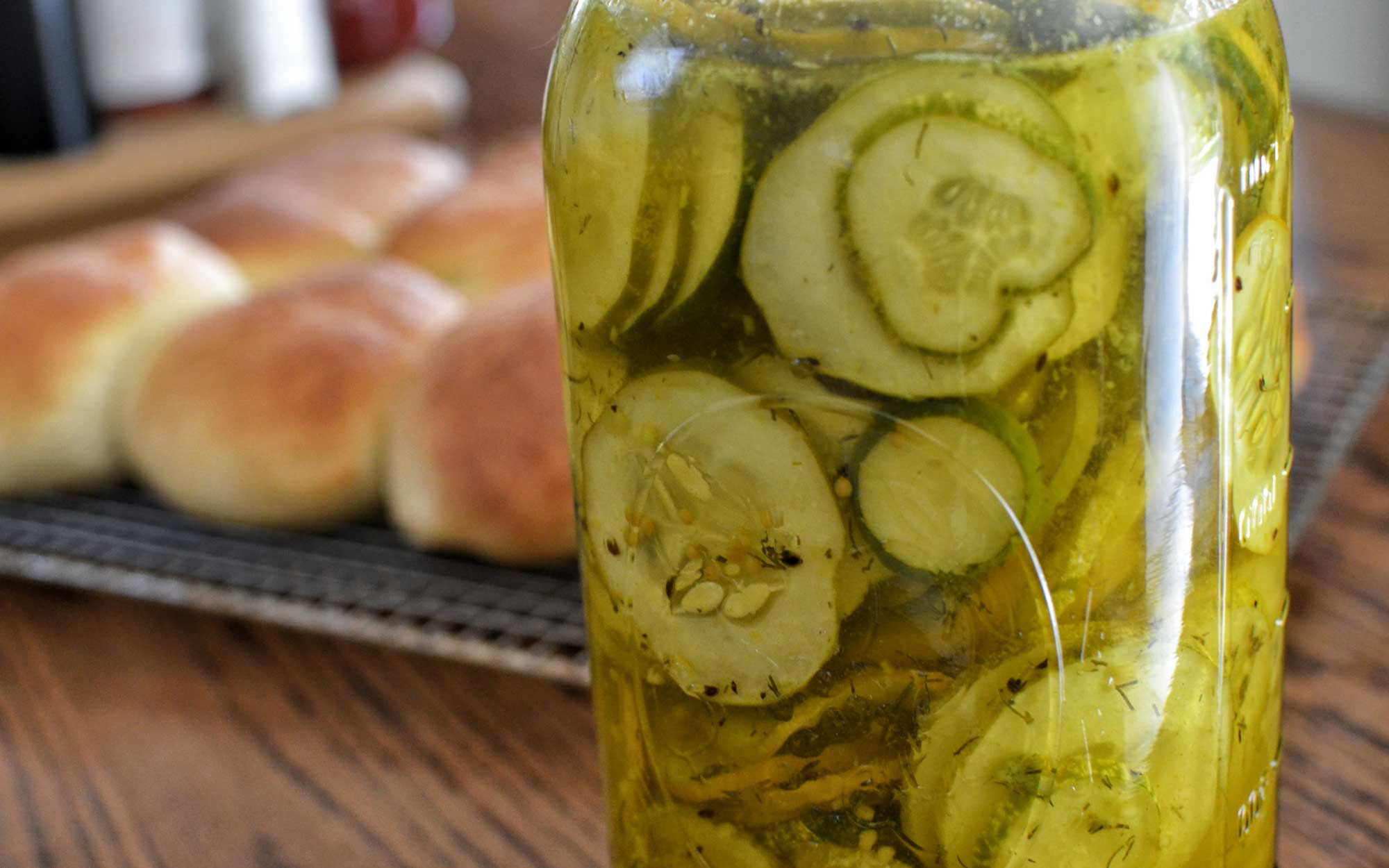 bread and butter pickles in a jar in front of a tray of baked rolls. Courtesy: jeffreyw (CC BY 2.0)