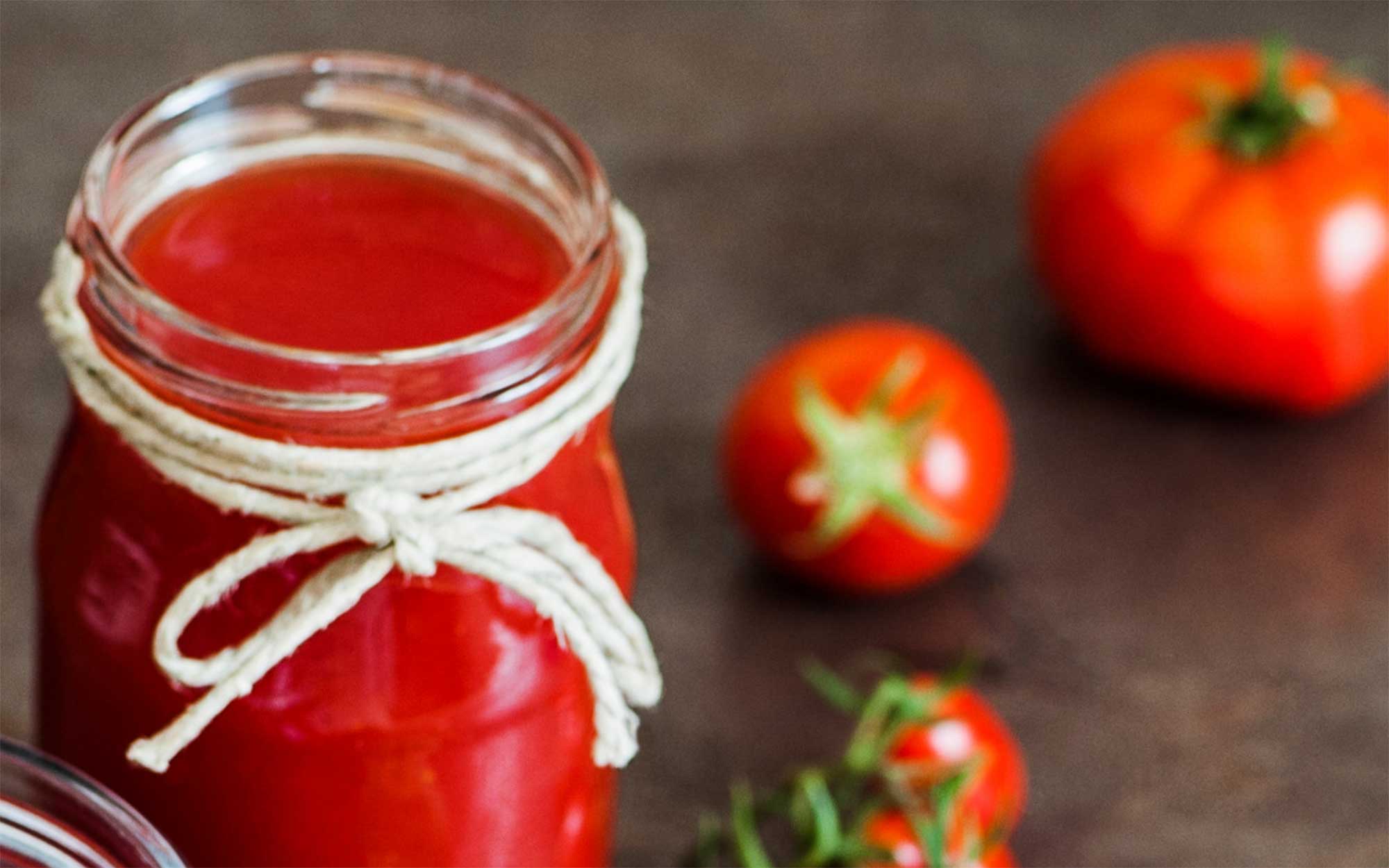 Fresh tomatoes near a jar of tomato juice.