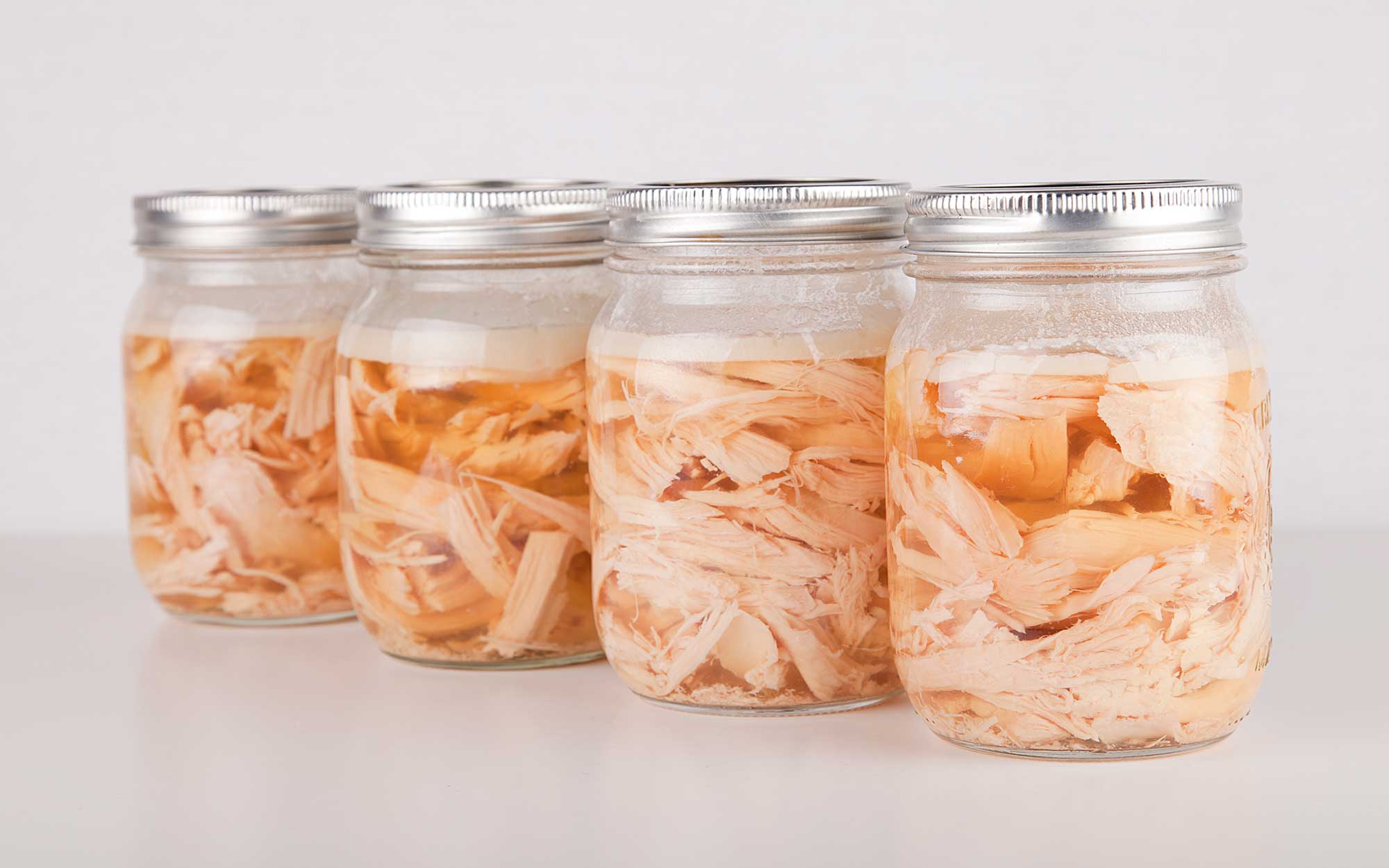 Four jars of home-canned chicken on a white countertop.