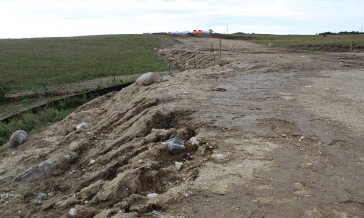 A long dirt road running through grassland to a wind energy construction project.