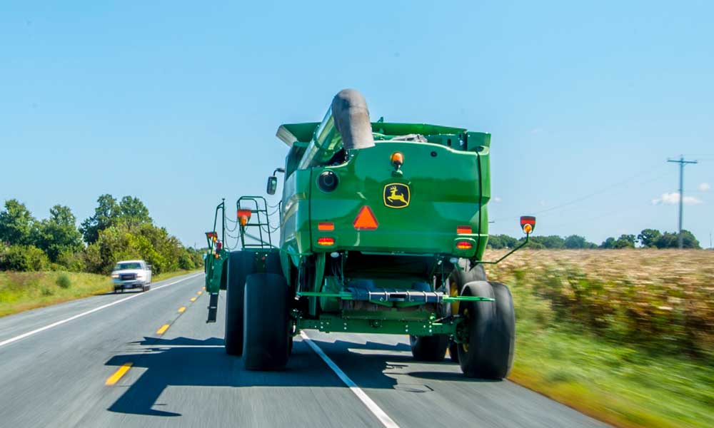 A green combine driving down a paved road.