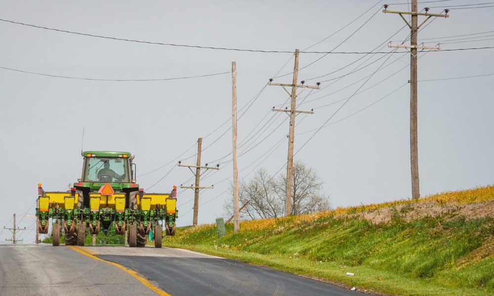 Green tractor driving down a road with low-hanging powerlines across it.