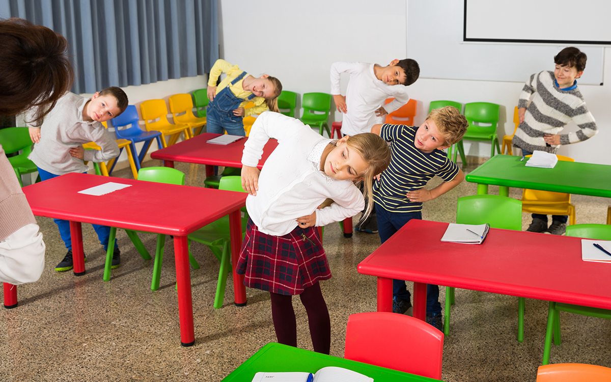 Portrait of schoolchildren with teacher performing daily physical exercises in classroom during break on lesson