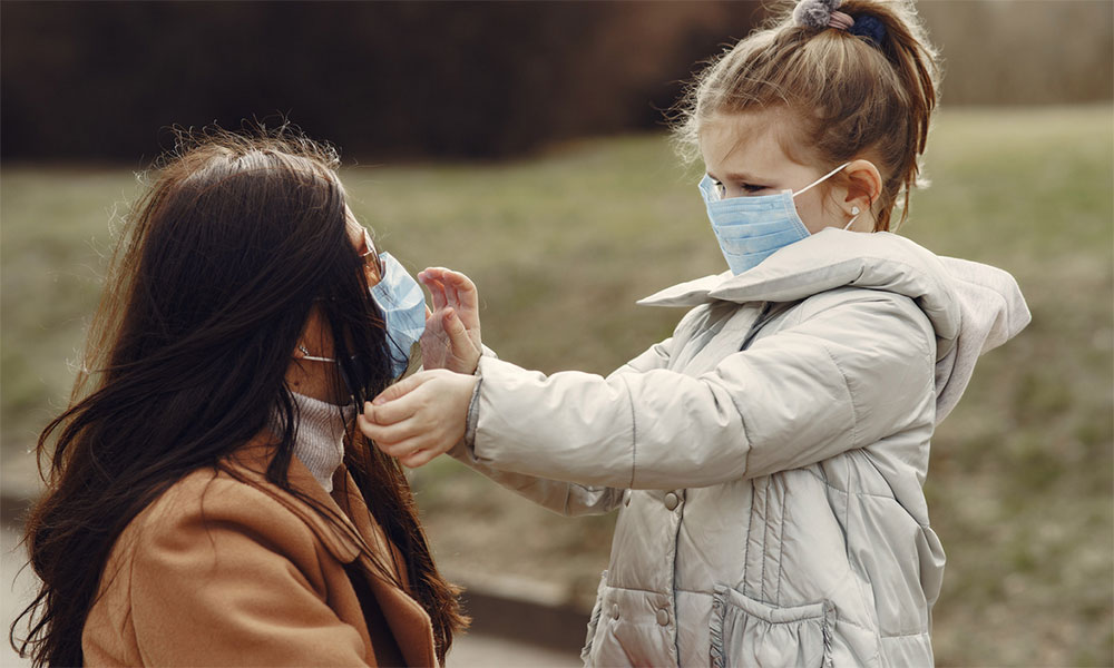 Mother and young daughter wearing masks in an outdoor park.