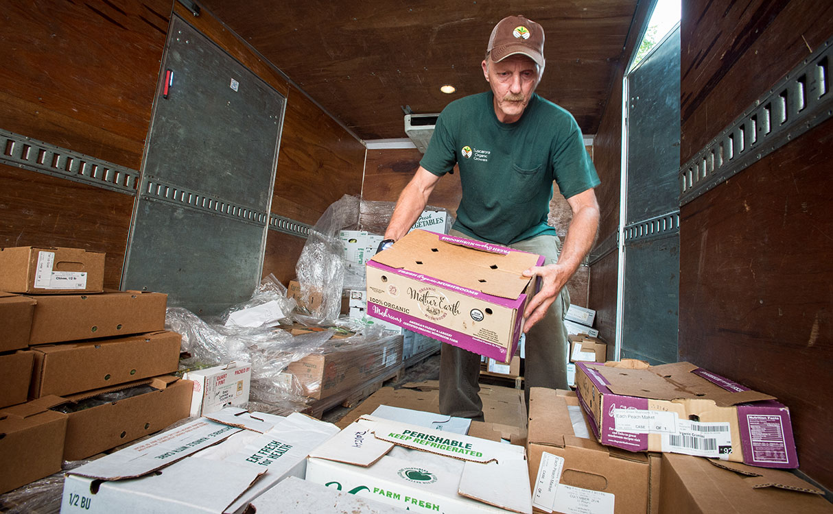 Producer unloading fresh, farm-grown produce from a delivery truck at a super market.