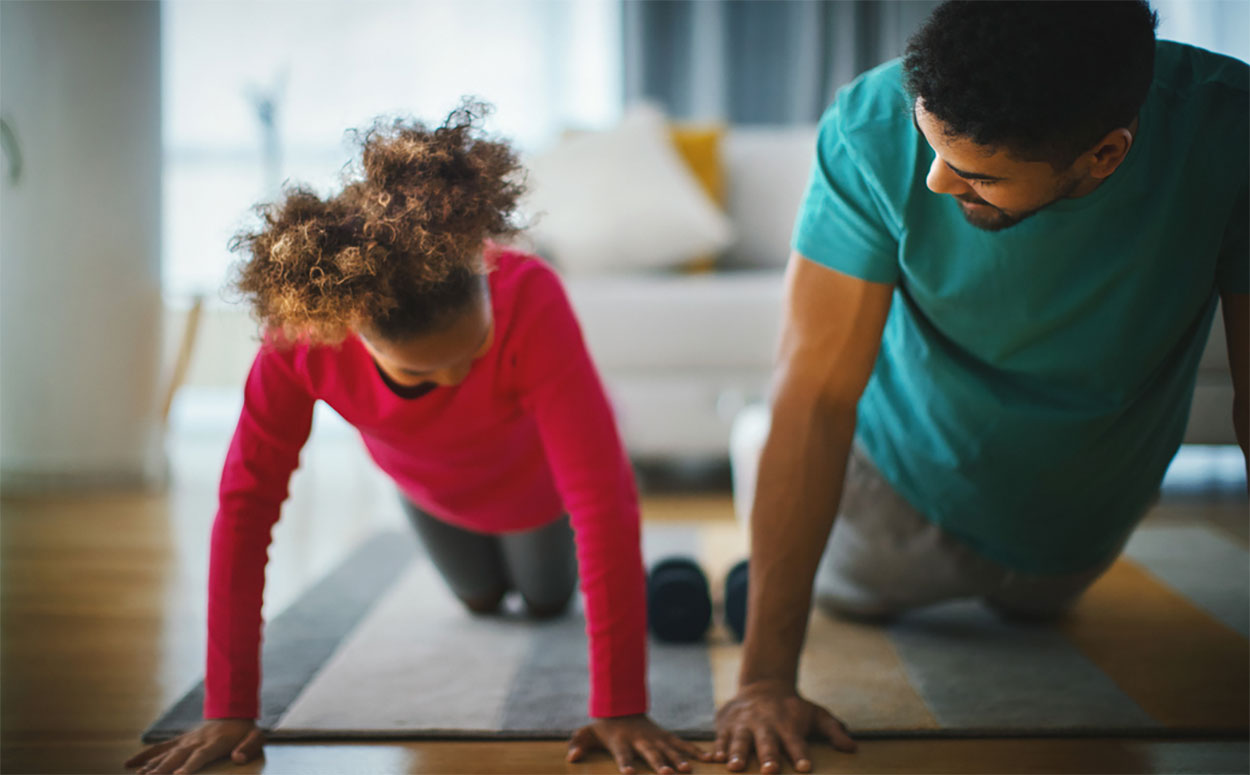 Father and daughter doing pushups on living room floor.