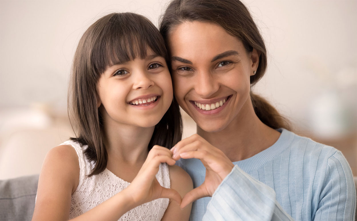Daughter and happy mother join hands in heart shape.
