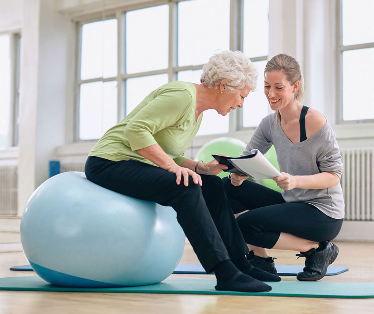 Senior woman and health coach looking at a health report in a gym.