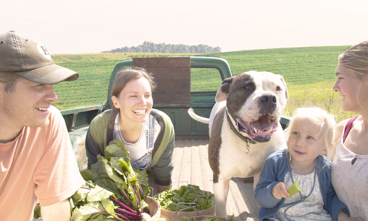 Young producers sampling produce outside a field with a young mother and her daughter.