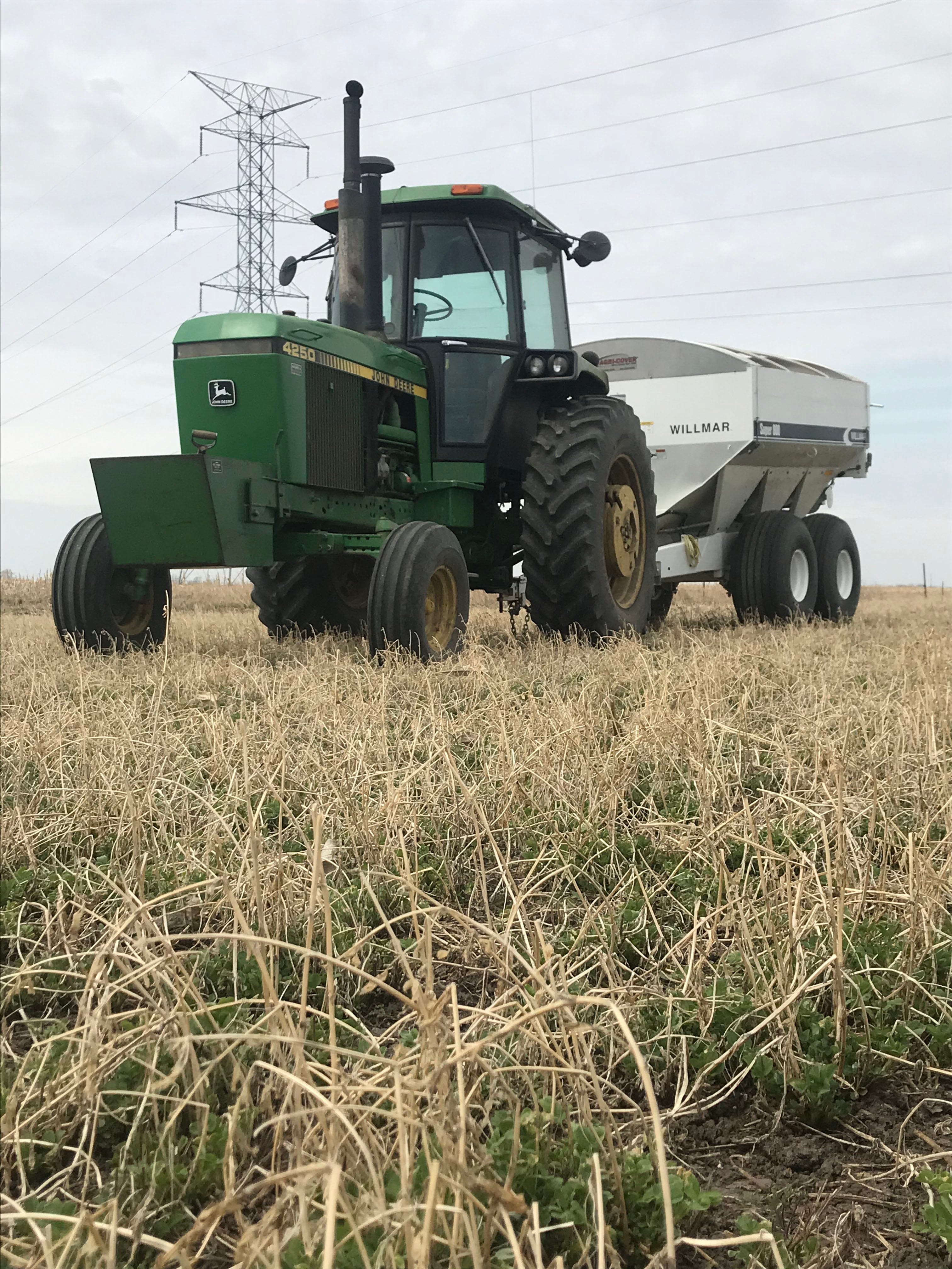 a green tractor pulling a white manure spreader in a field