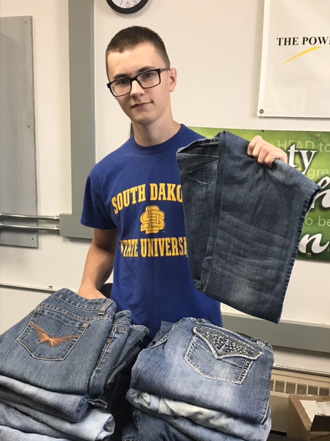 a young man standing in front of a stack of blue jeans, holding a pair of blue jeans up.