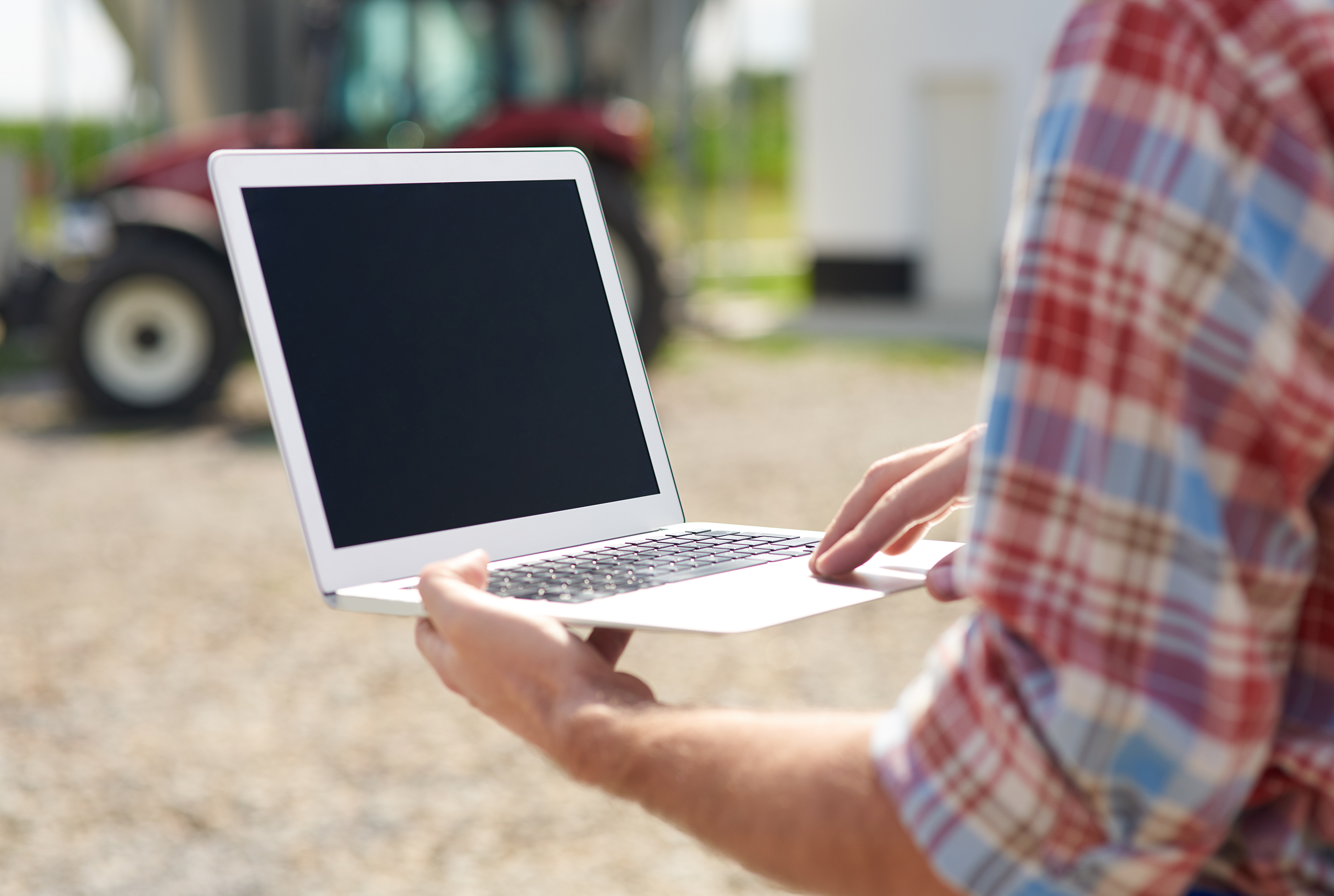 a person in a red and blue plaid shirt holding a laptop outdoors