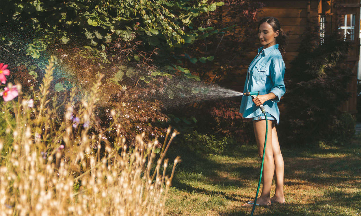 Young woman watering a drought-stressed flower garden.