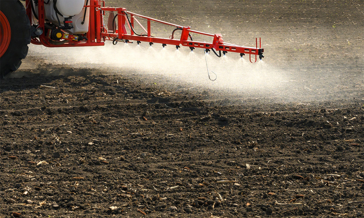 Tractor spraying pre-emergent herbicide in a bare field.