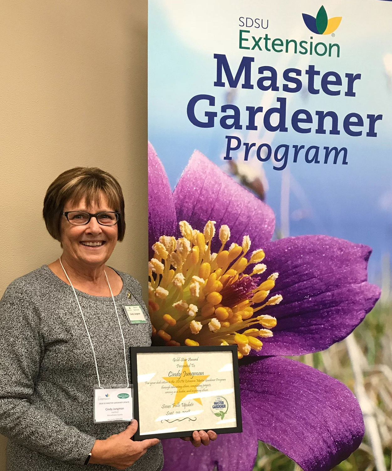 Cindy Jungman holding an award in front of an SDSU Extension Master Gardener Program banner.