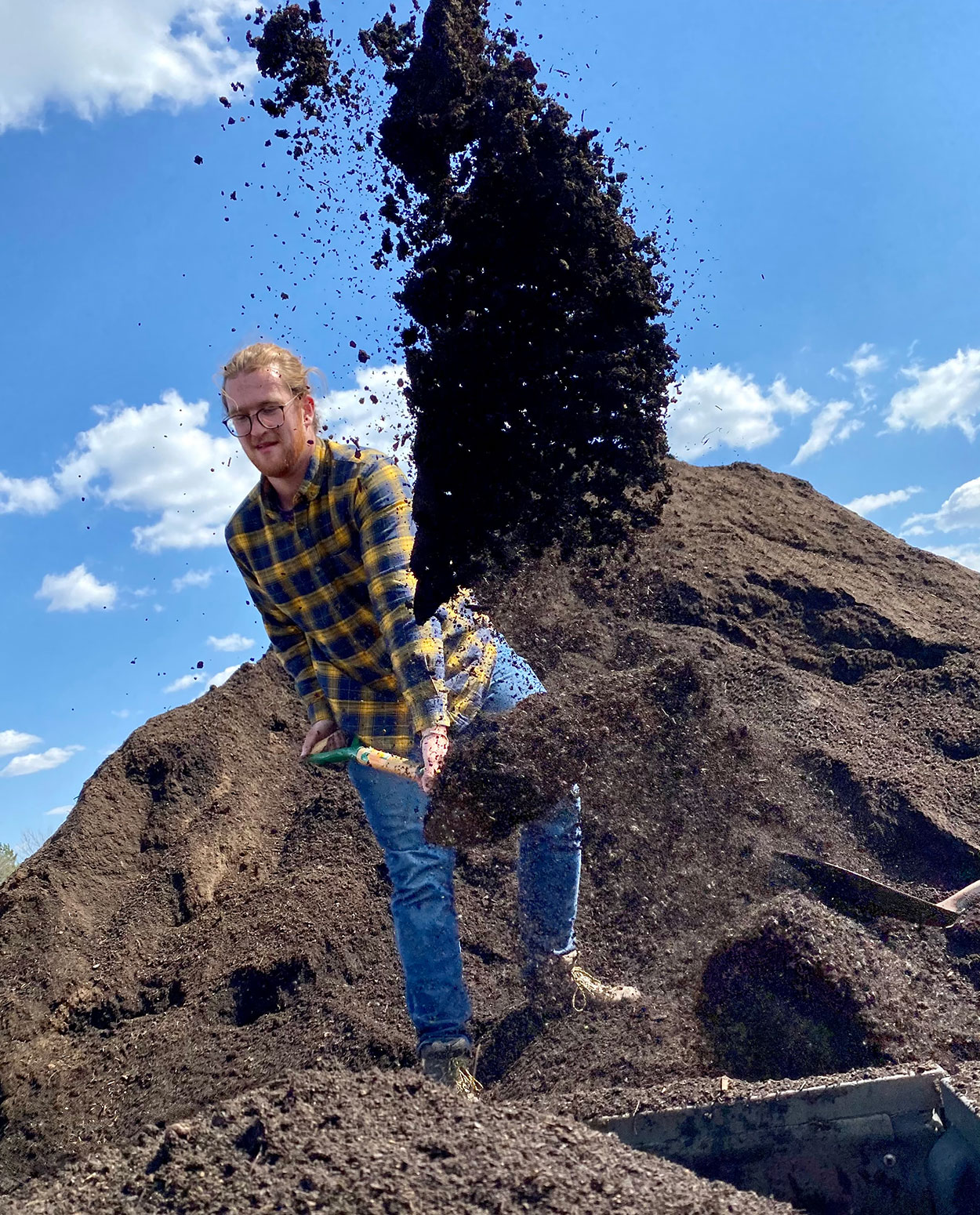 Young man shoveling a pile of compost.