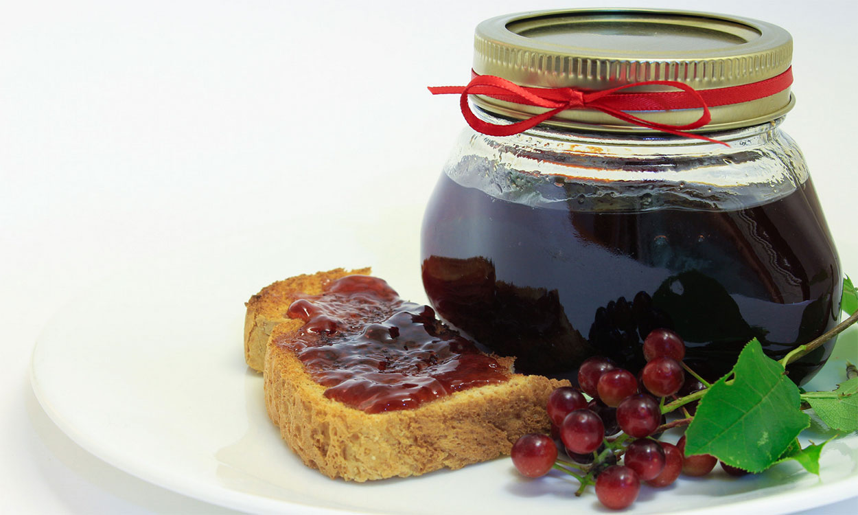 Jar of chokecherry jam next to a piece of toast with jam.