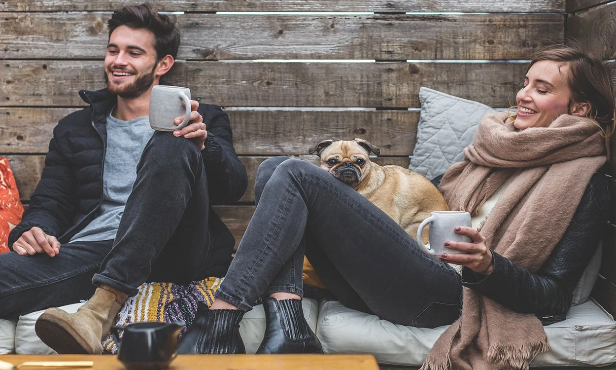 A couple having a conversation while drinking coffee with their dog.