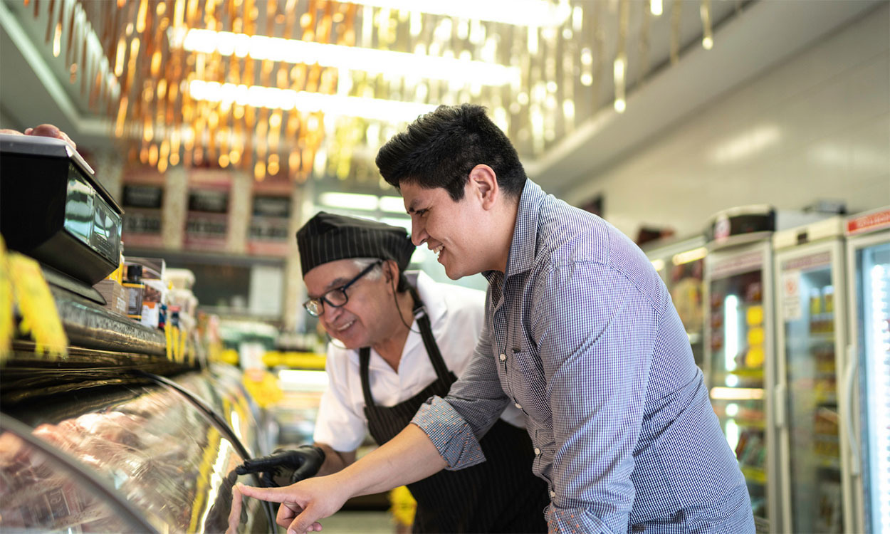 Butcher helping a customer select meat in a glass cabinet.